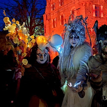 Die drei kostümierten Hexen in aufwendigen Kostümen vor der orange angestrahlten Burg.