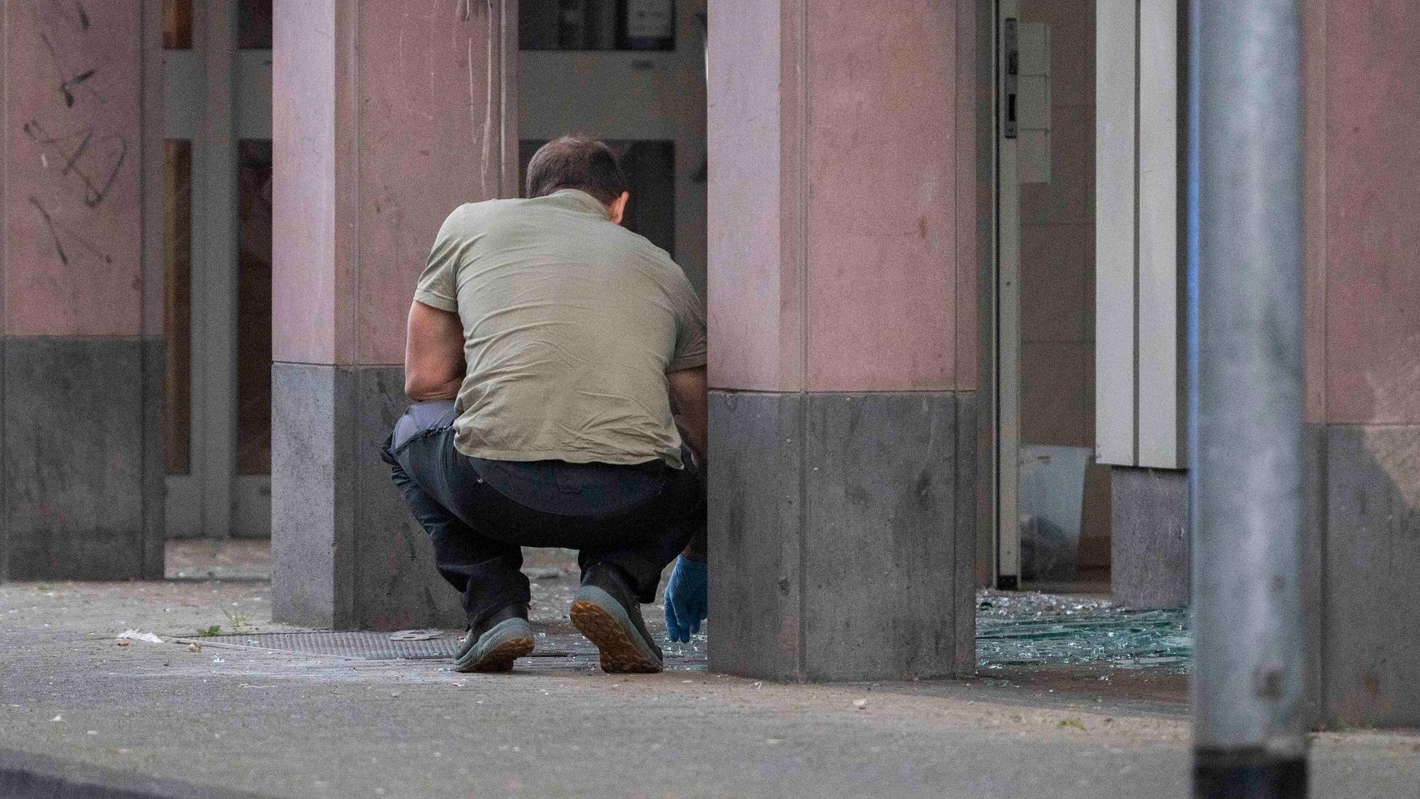 Das Bild zeigt einen Beamten, der mit Einweghandschuhen in Glassplittern nach Spuren sucht.