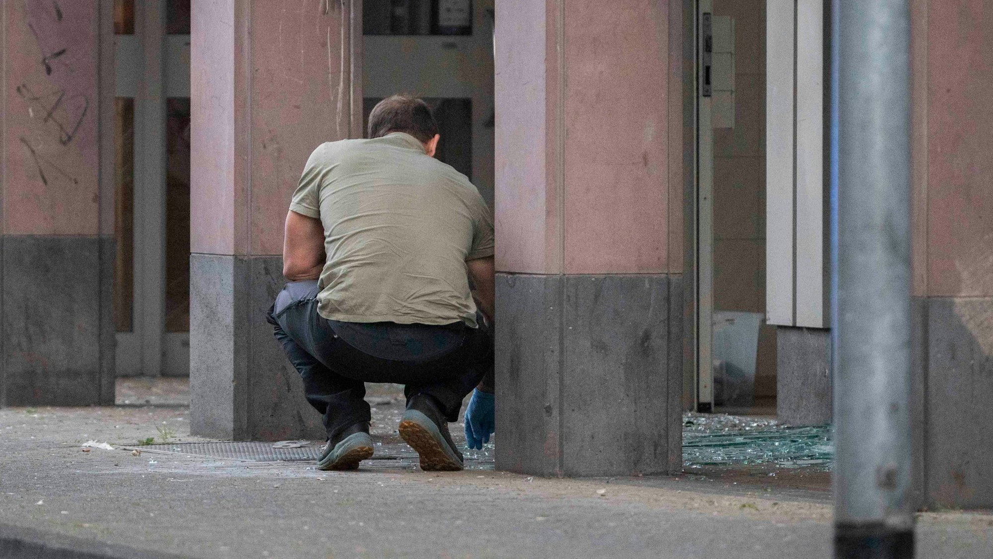 Das Bild zeigt einen Beamten, der mit Einweghandschuhen in Glassplittern nach Spuren sucht.