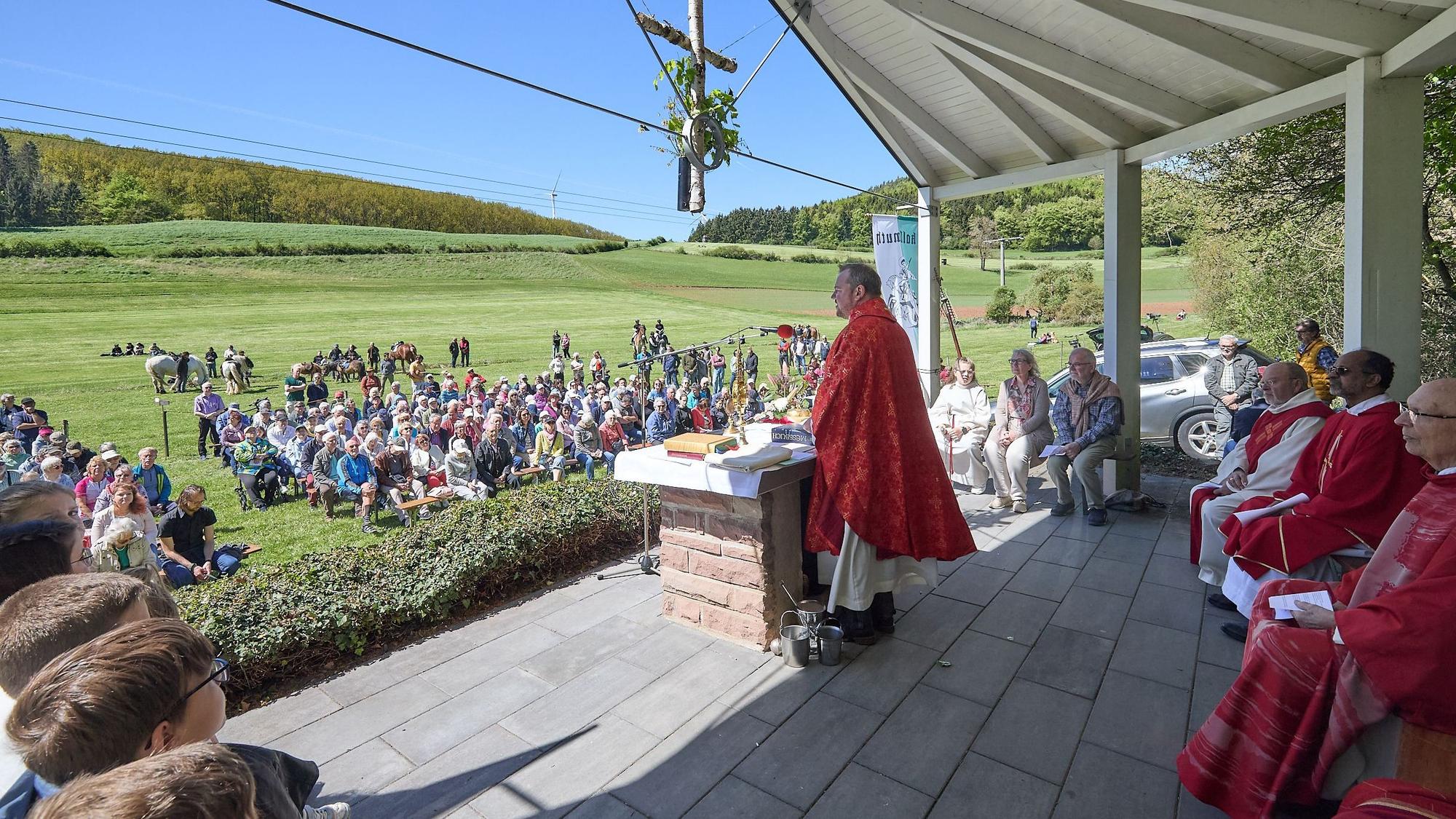 Am Altar vor der Festwiese steht der Pfarrer, die übrigen Kirchenvertreter sitzen hinter ihm. Auf der Wiese sitzen zahlreiche Gottesdienstteilnehmer.