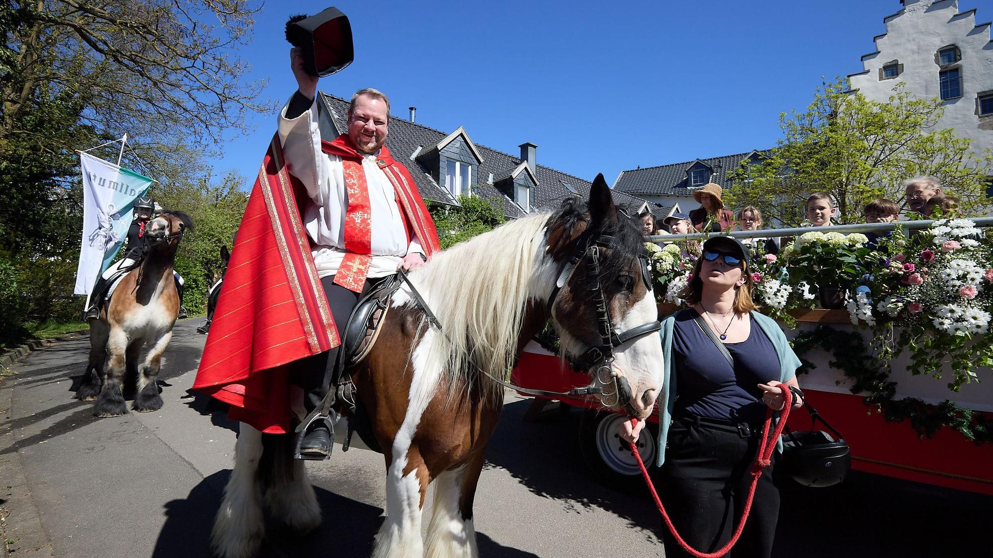 Hoch zu Ross grüßt der Pfarrer mit dem gelupften Birett.