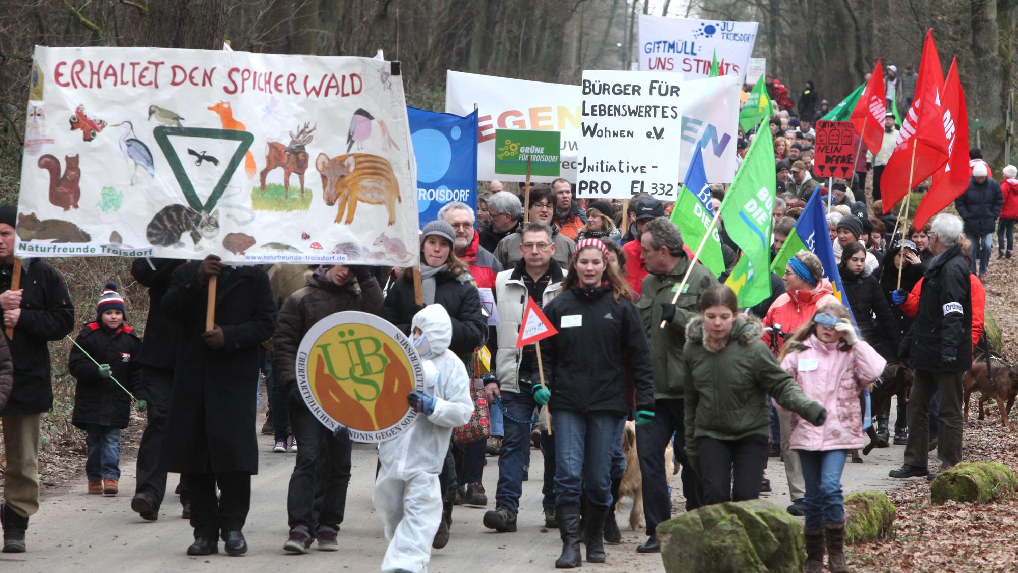 Menschen mit Protesttransparenten auf einer Straße im Wald.