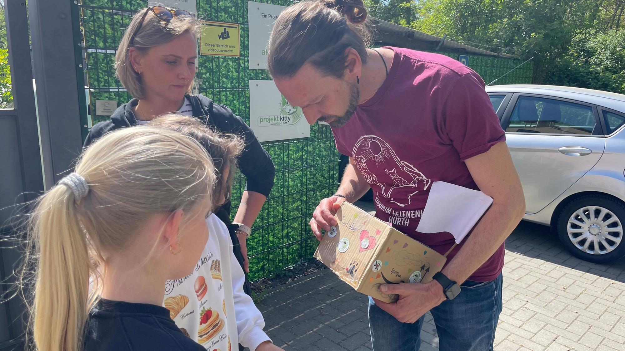 Das Foto zeigt einen Mann mit einer Spendenbox, daneben eine junge Frau und ein Mädchen.