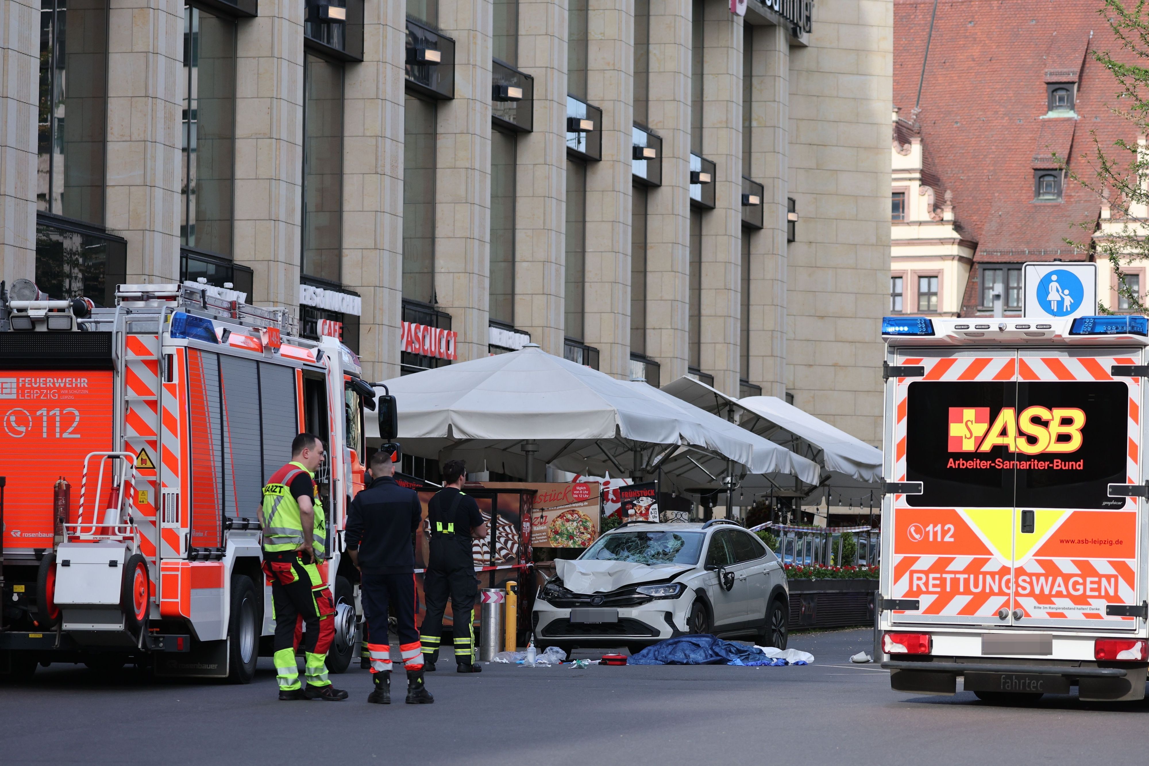 Rettungskräfte stehen in der Nähe eines beschädigten Autos an der Stelle, wo ein Auto in eine Menschengruppe gefahren ist.