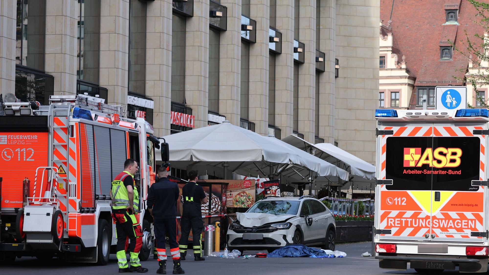 Rettungskräfte stehen in der Nähe eines beschädigten Autos an der Stelle, wo ein Auto in eine Menschengruppe gefahren ist.