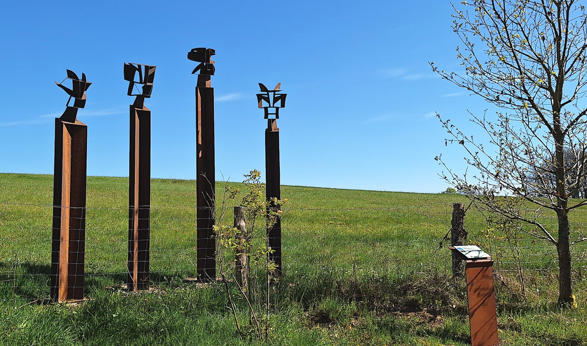 Das Bild zeigt ein Kunstwerk auf dem Rundweg. Vier Stehlen ragen in den Himmel.
