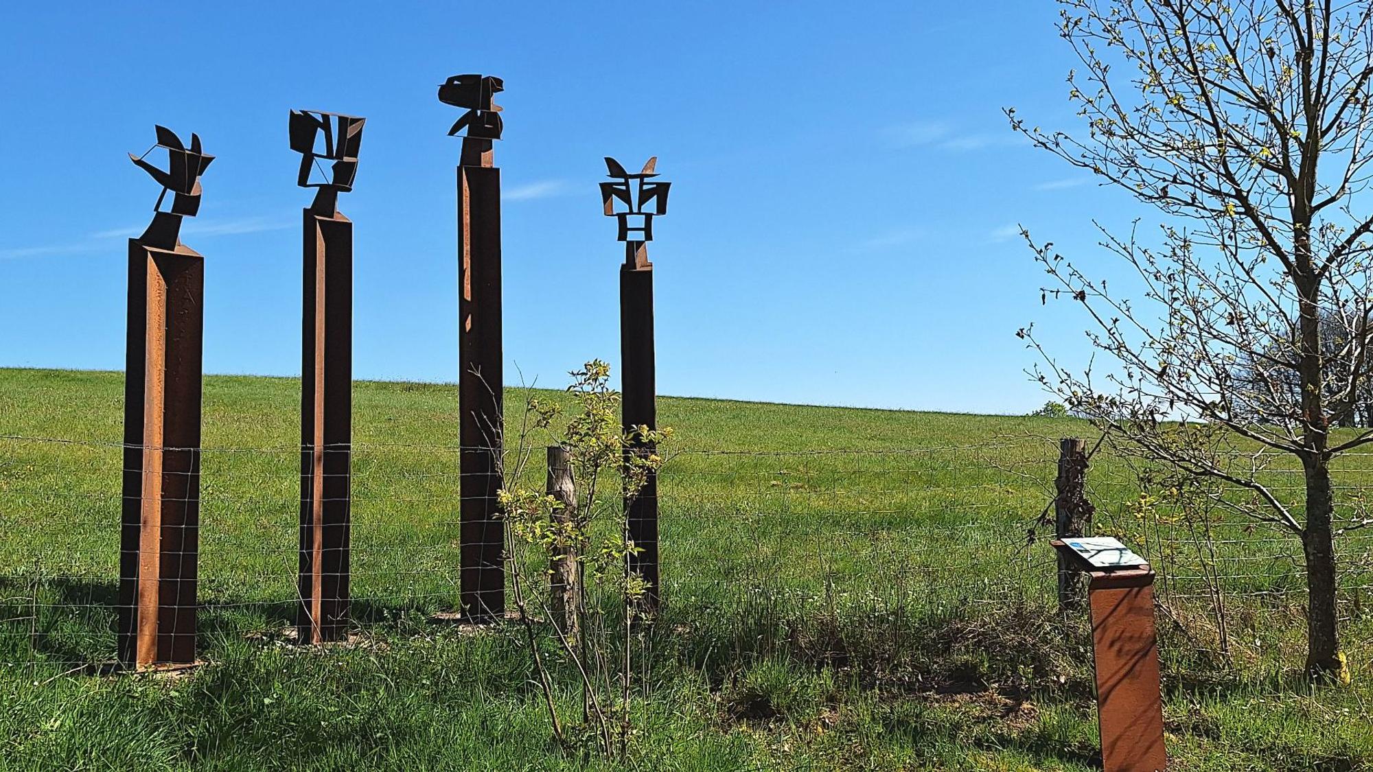 Das Bild zeigt ein Kunstwerk auf dem Rundweg. Vier Stehlen ragen in den Himmel.