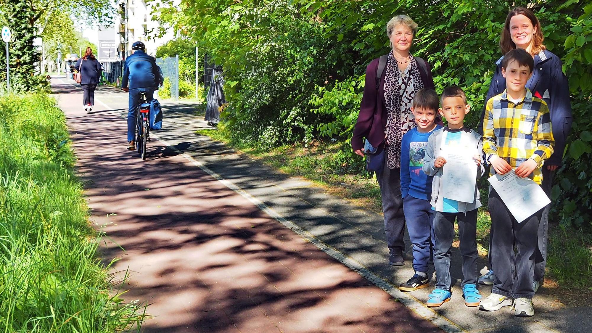 Drei Kinder und zwei Frauen stehen am Rand eines Radwegs.