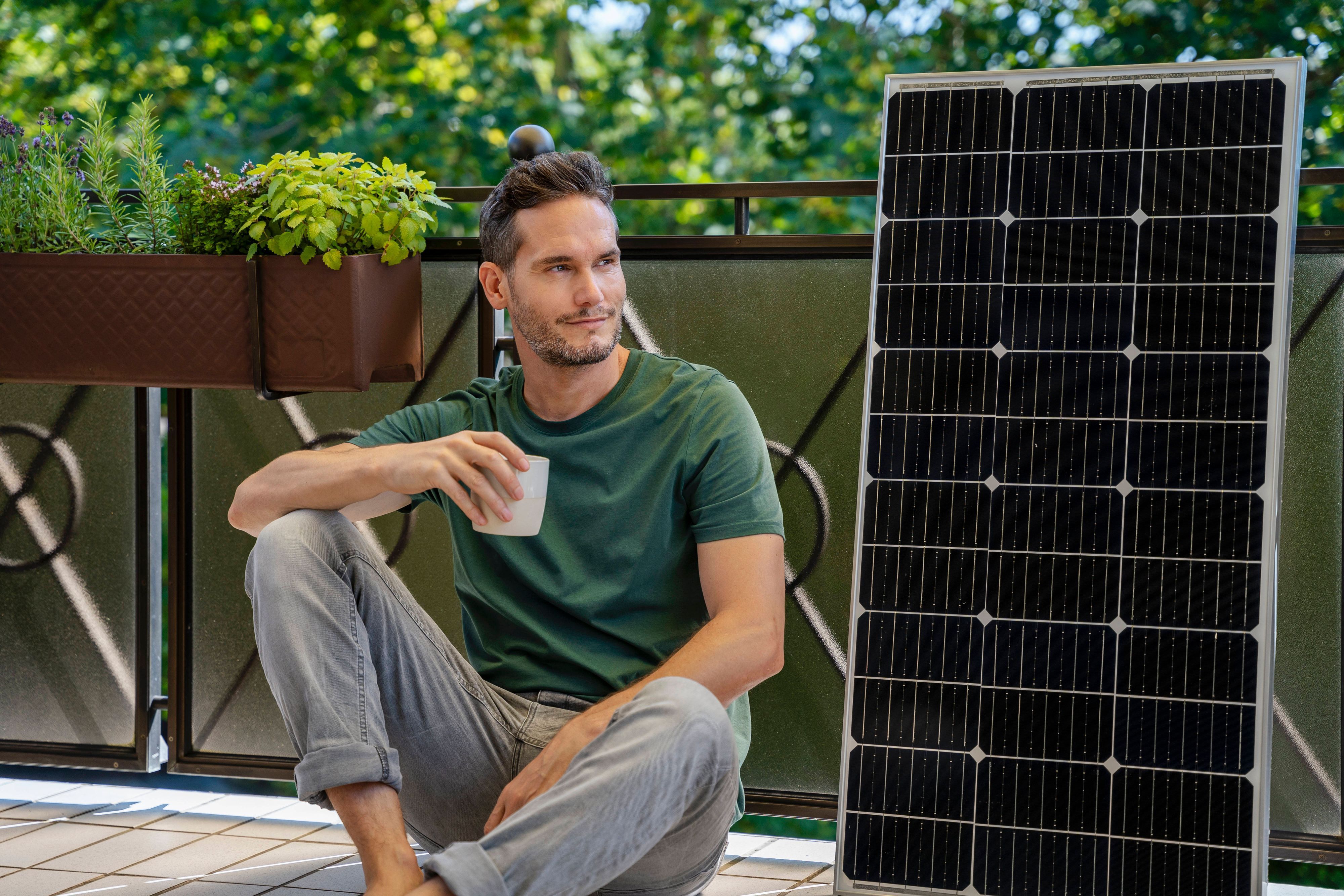 Mann mit Kaffee, Solarmodul und Pflanzen auf Balkon