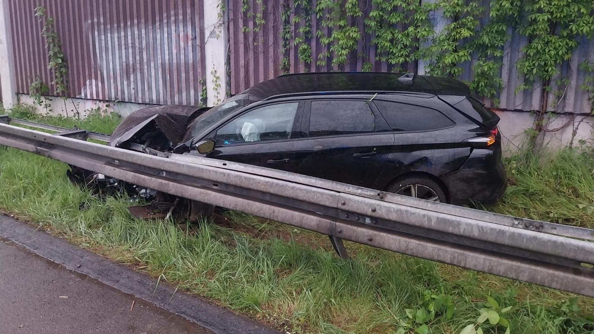 Ein dunkler Kombi steht im Gras hinter der Leitplanke einer Autobahn. Die Motorhaube ist zerbeult.