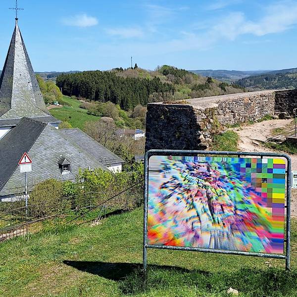 Das Bild zeigt ein Kunstwerk. Im Hintergrund ist die Ruine des Bergfrieds der Kronenburger Burg zu sehen.