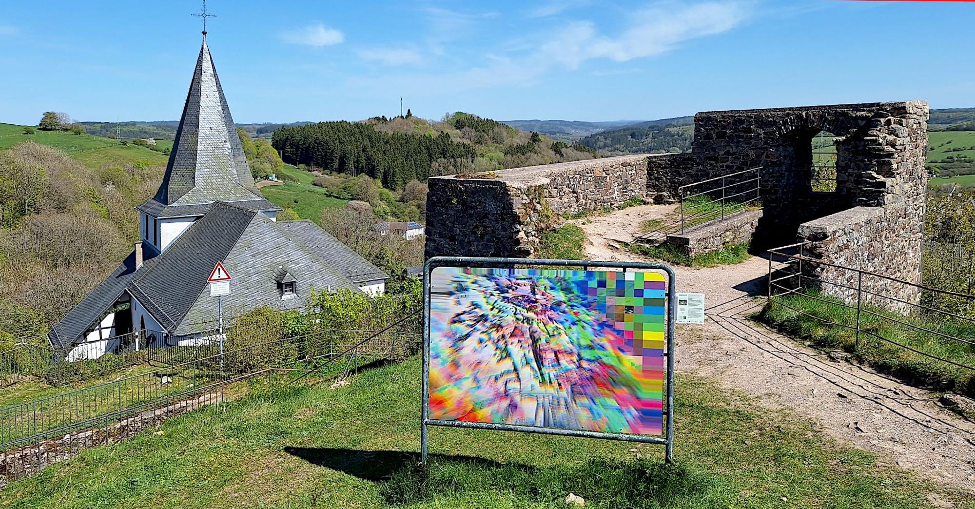 Das Bild zeigt ein Kunstwerk. Im Hintergrund ist die Ruine des Bergfrieds der Kronenburger Burg zu sehen.