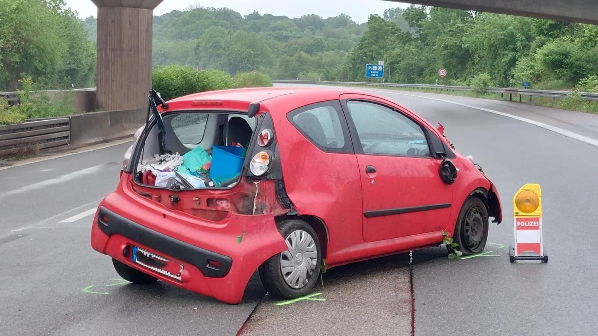 Ein roter Kleinwagen steht mit zerstörtem Heck auf dem Mittelstreifen einer Autobahn.