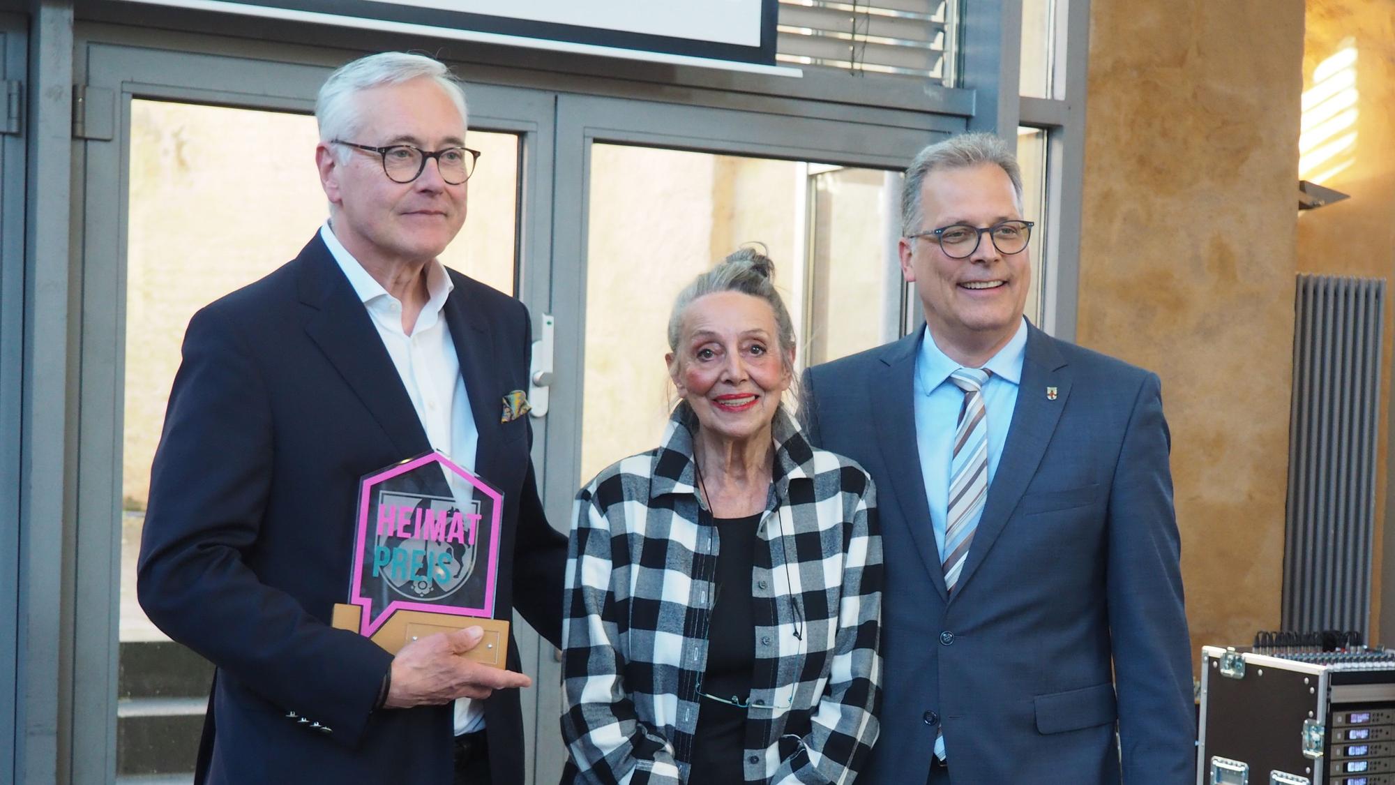 Ralf Engels, Margrit Adams-Scheuer und Bürgermeister Ulf Hürtgen stehen nebeneinander, Engels hält die gläserne Trophäe.