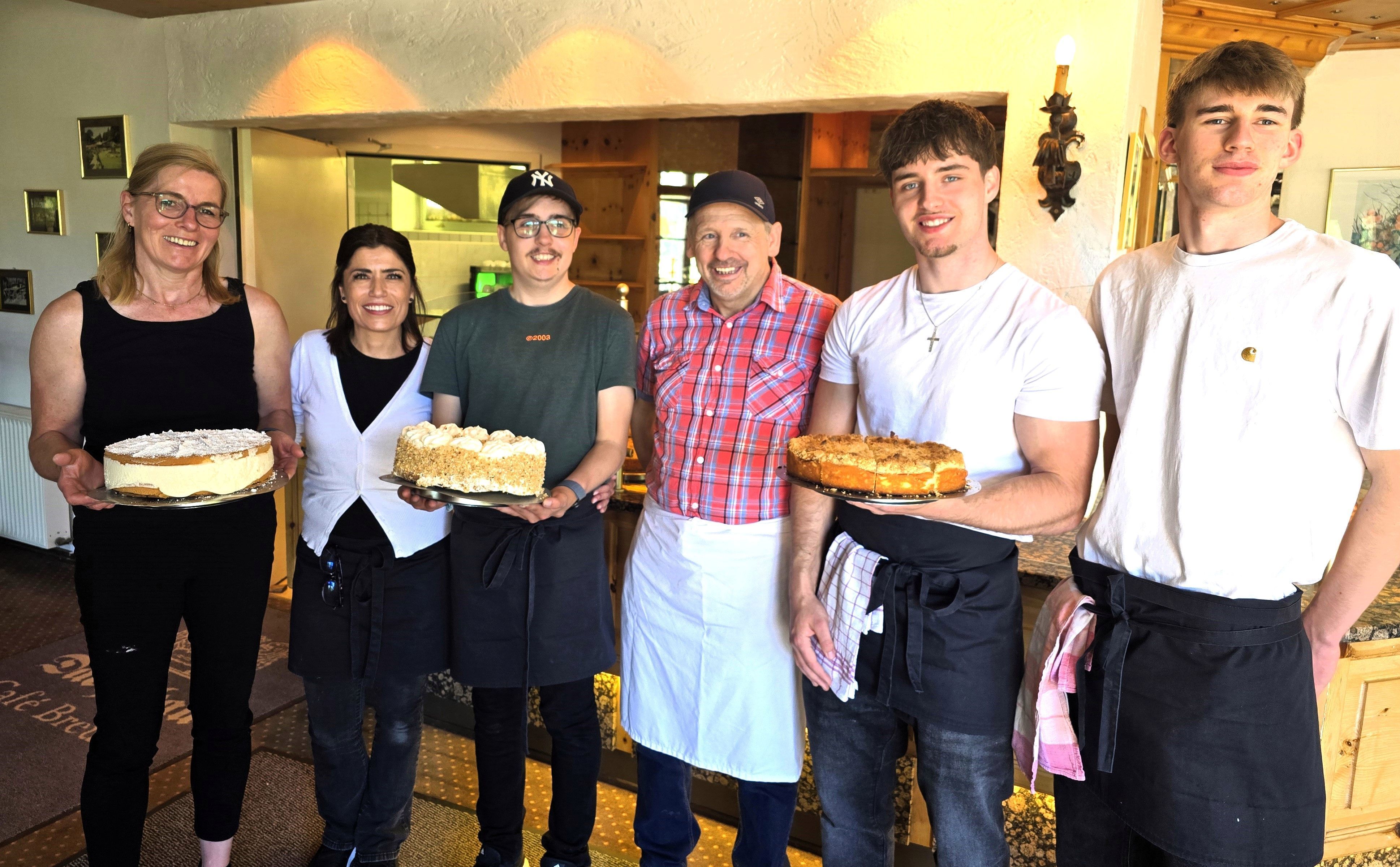 Sechs Menschen stehen nebeneinander, drei von ihnen halten Kuchen in der Hand.