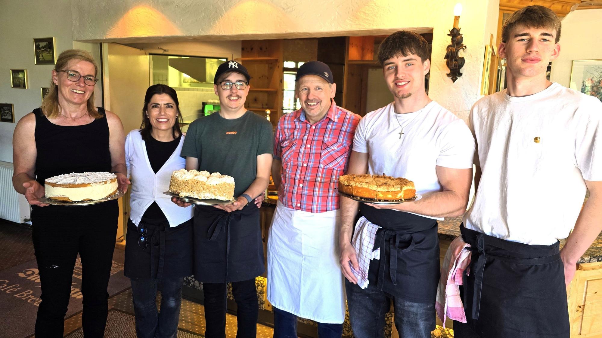 Sechs Menschen stehen nebeneinander, drei von ihnen halten Kuchen in der Hand.