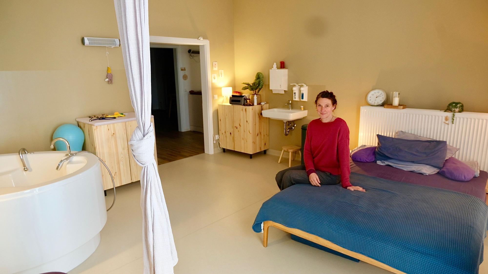 Eine Frau sitzt auf dem großen Bett einem geräumigen Zimmer, in dem auch eine Badewanne steht.