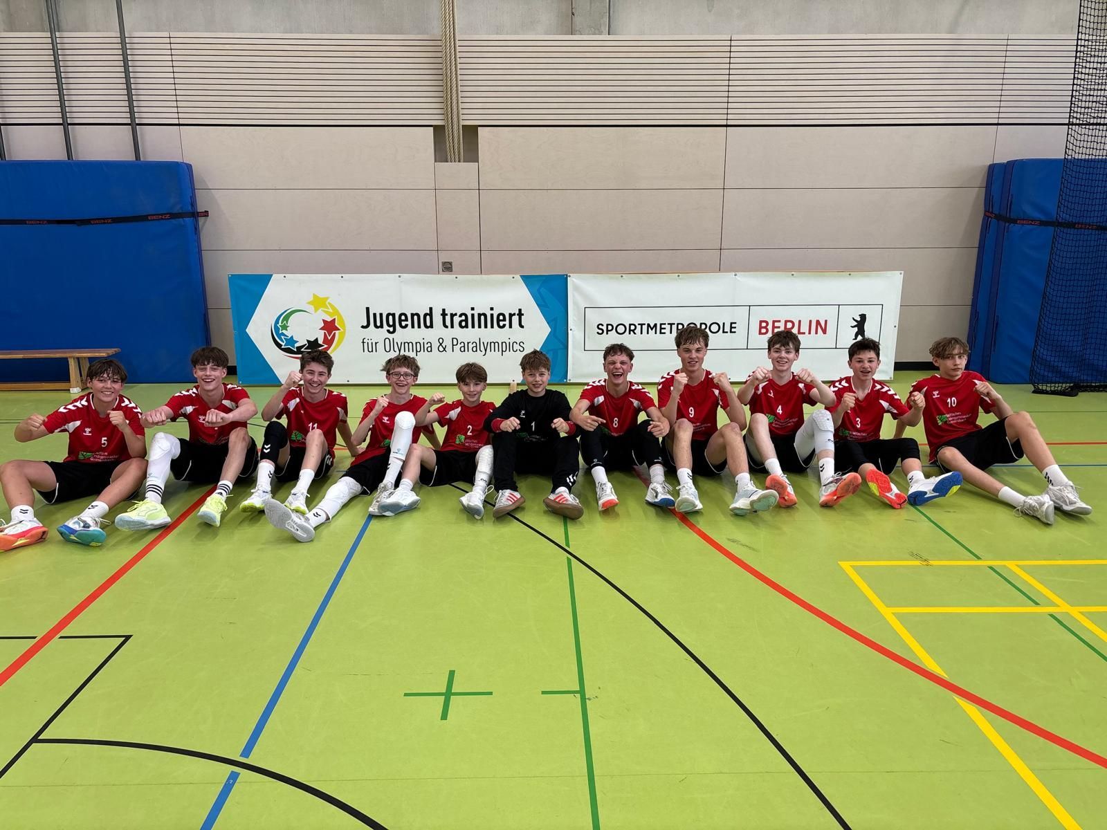Die Handballer sitzen auf dem Hallenboden und recken die Fäuste.