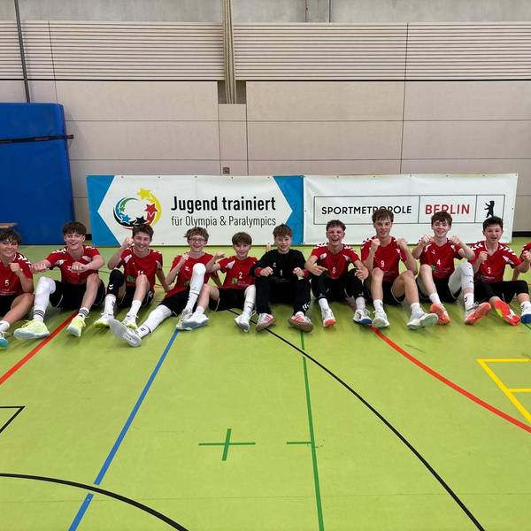 Die Handballer sitzen auf dem Hallenboden und recken die Fäuste.