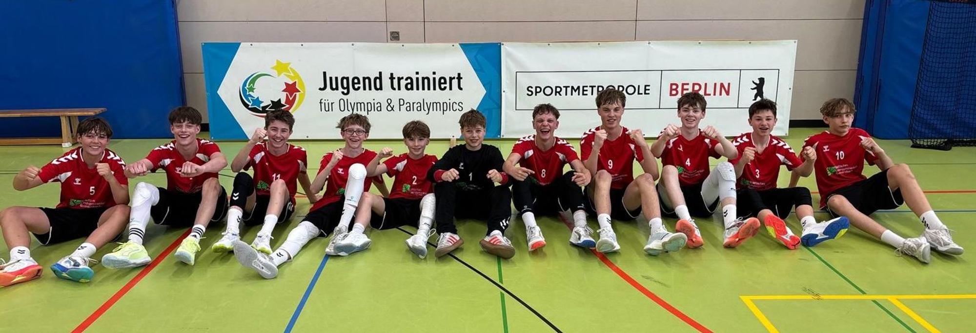 Die Handballer sitzen auf dem Hallenboden und recken die Fäuste.