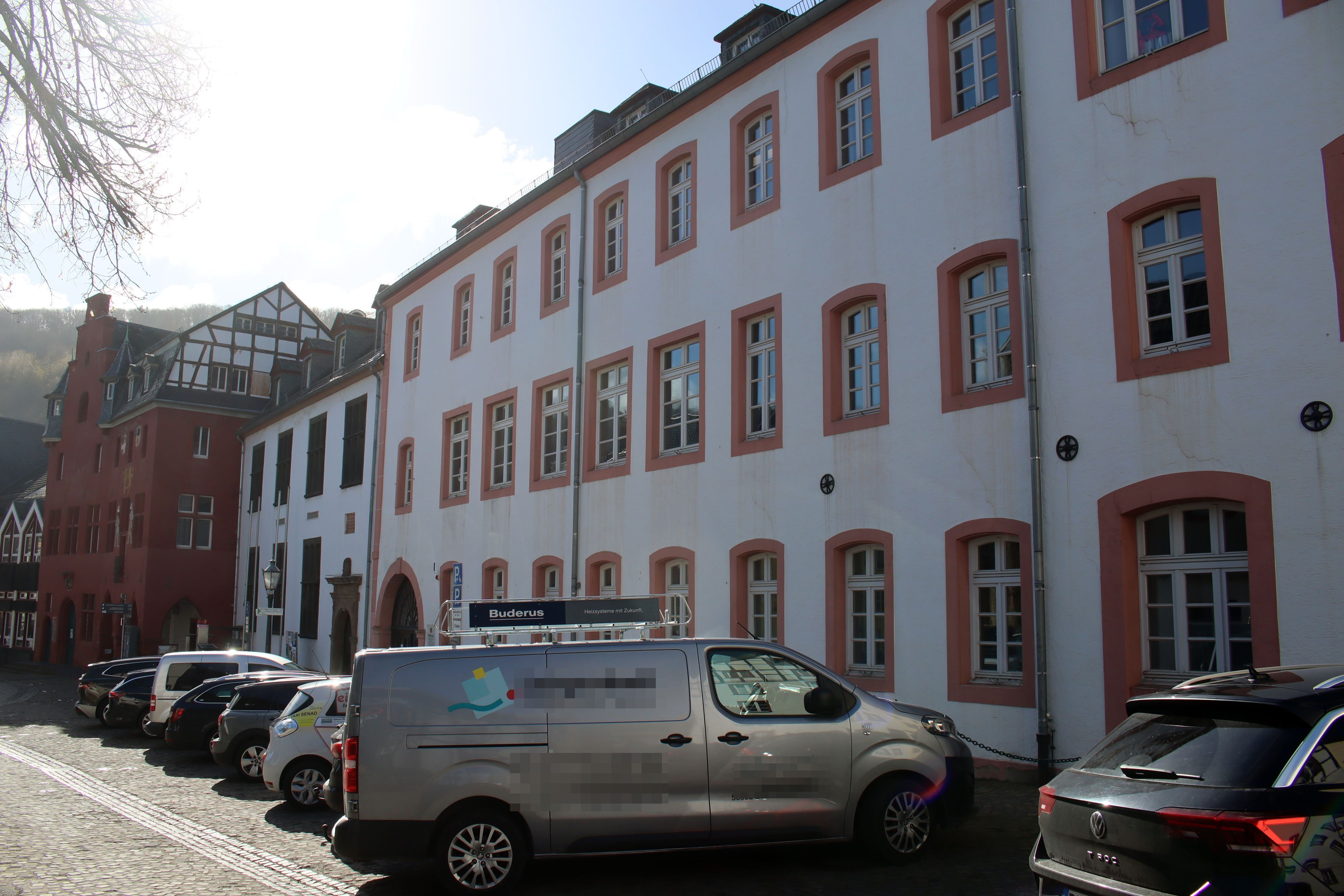 Autos stehen vor dem Grundschulgebäude. Im Hintergrund ist das benachbarte Rathaus zu erkennen.
