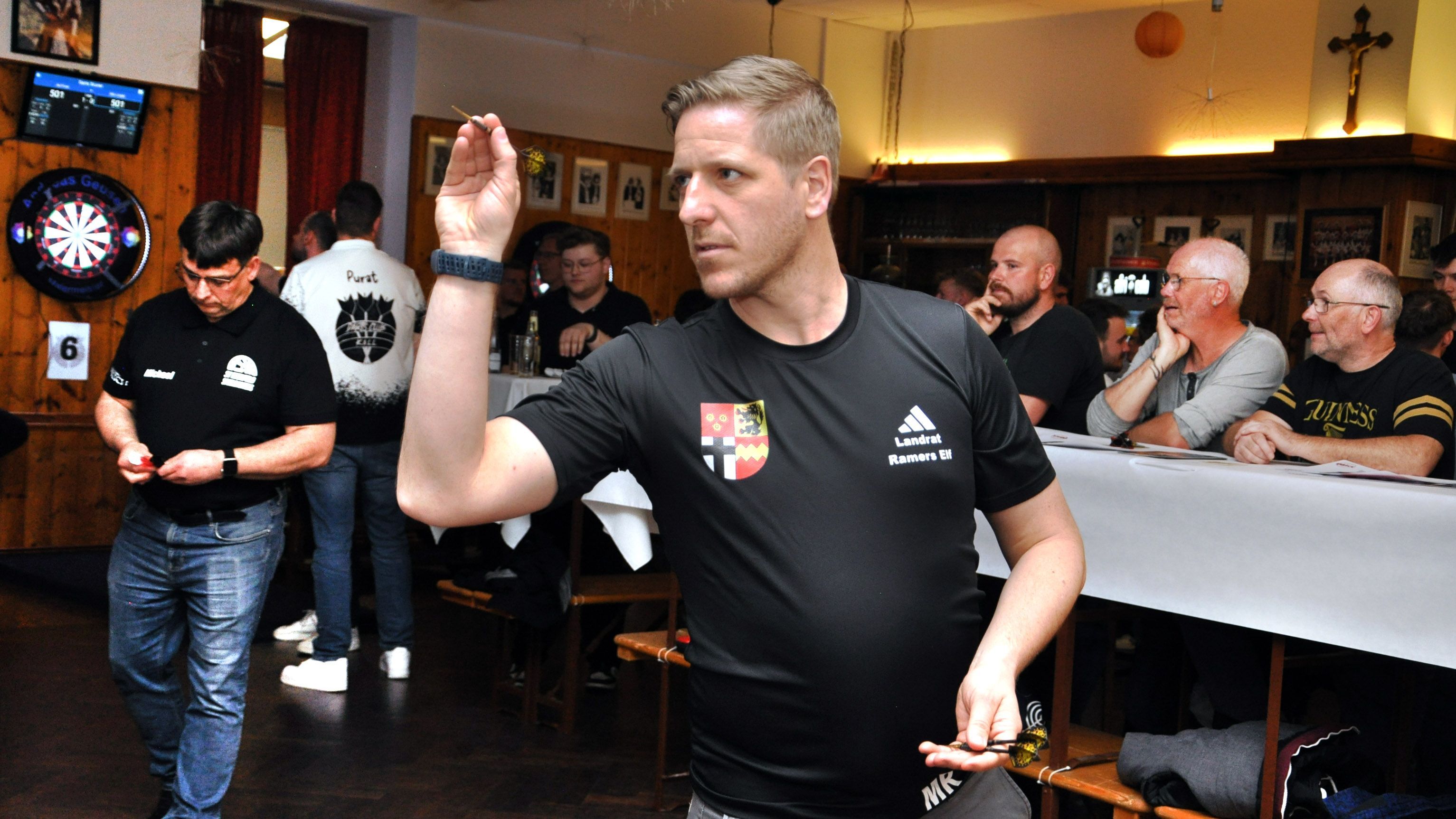Landrat Markus Ramers im schwarzen T-Shirt mit Kreis-Wappen beim Dartturnier in Kall.