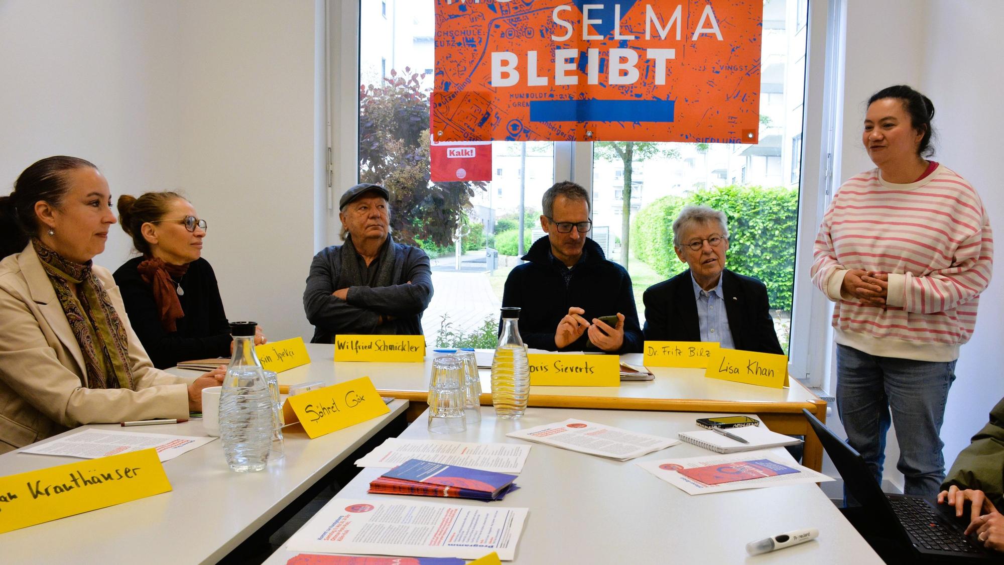 Eine Gruppe von Menschen sitzt hinter Namensschildern an einem Tisch.