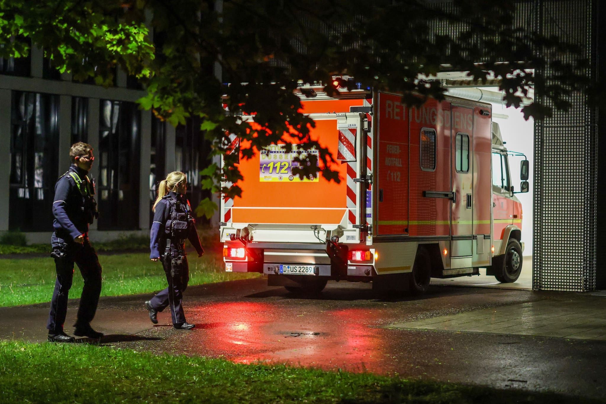Polizisten laufen an einem ankommenden Rettungswagen vorbei, der eine deutsche Patientin in das Infektionszentrum der Uniklinik Düsseldorf bringt.