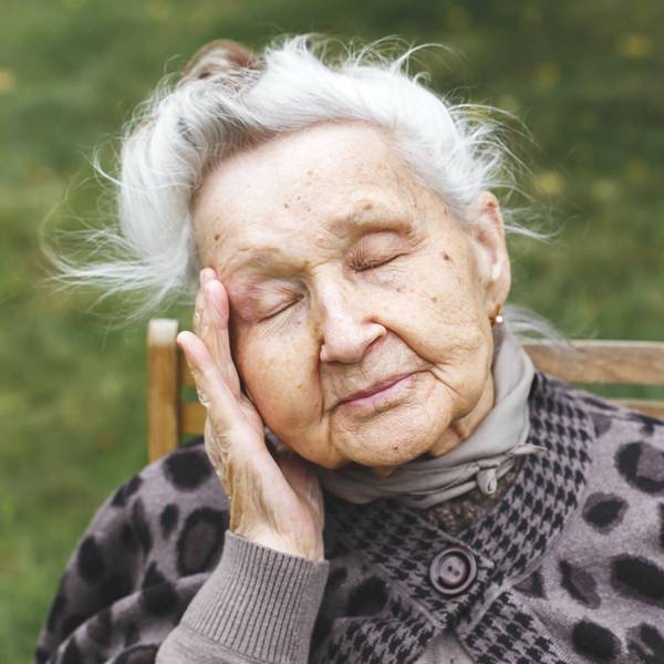 Ältere Frau mit geschlossenen Augen, die ihren Kopf berührt, Müdigkeit oder Unwohlsein ausdrückt.
