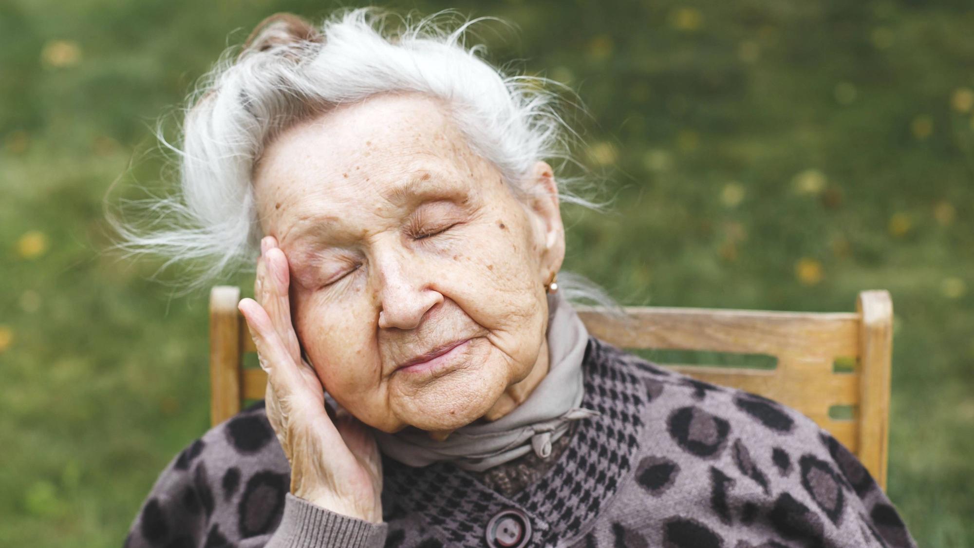 Ältere Frau mit geschlossenen Augen, die ihren Kopf berührt, Müdigkeit oder Unwohlsein ausdrückt.