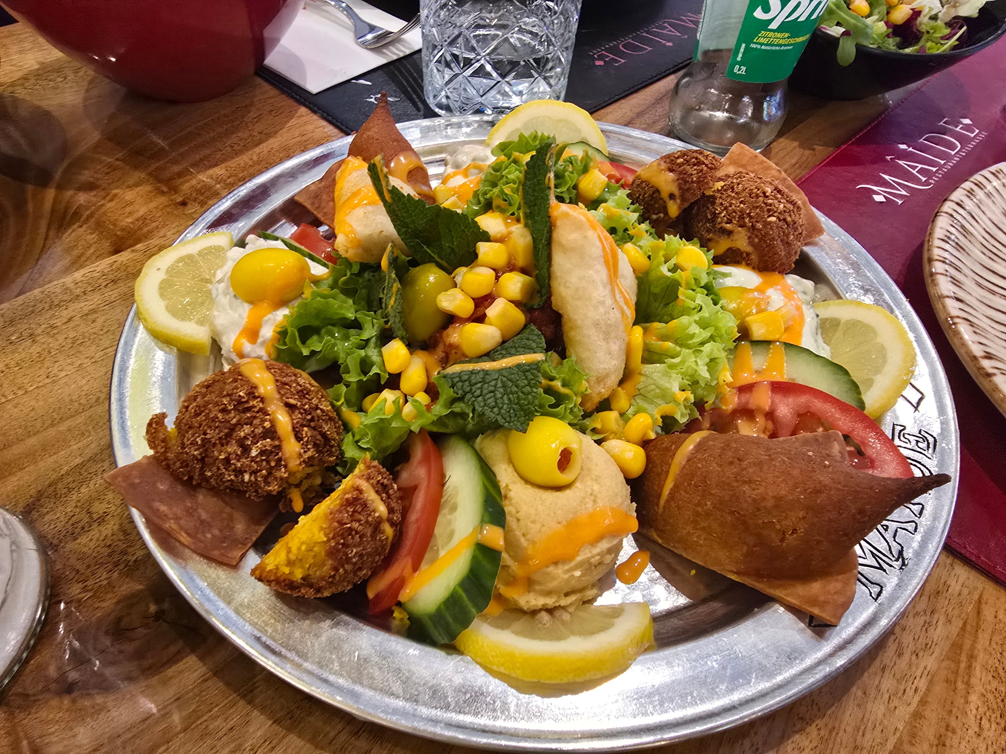 Die gemischte Vorspeisenplatte mit unterschiedlichen Dips und Falafel auf einem Teller mit Zitronenscheiben garniert.