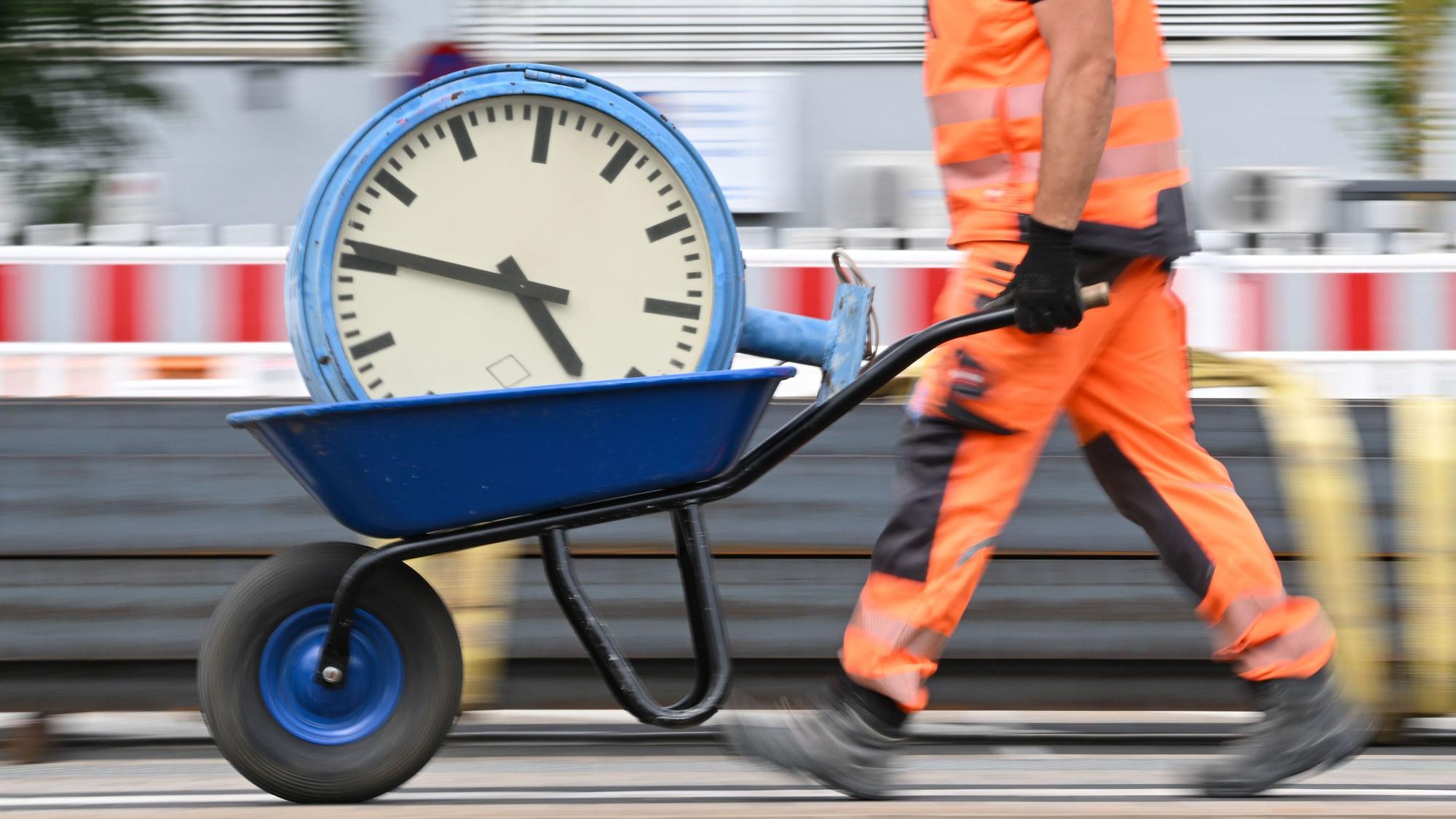 ARCHIV - 17.07.2024, Hessen, Mörfelden-Walldorf: Ein Arbeiter transportiert eine Bahnhofsuhr auf einer Schubkarre. (zu dpa: «Niedersachsen arbeiten 2025 drei Stunden weniger») Foto: Arne Dedert/dpa +++ dpa-Bildfunk +++