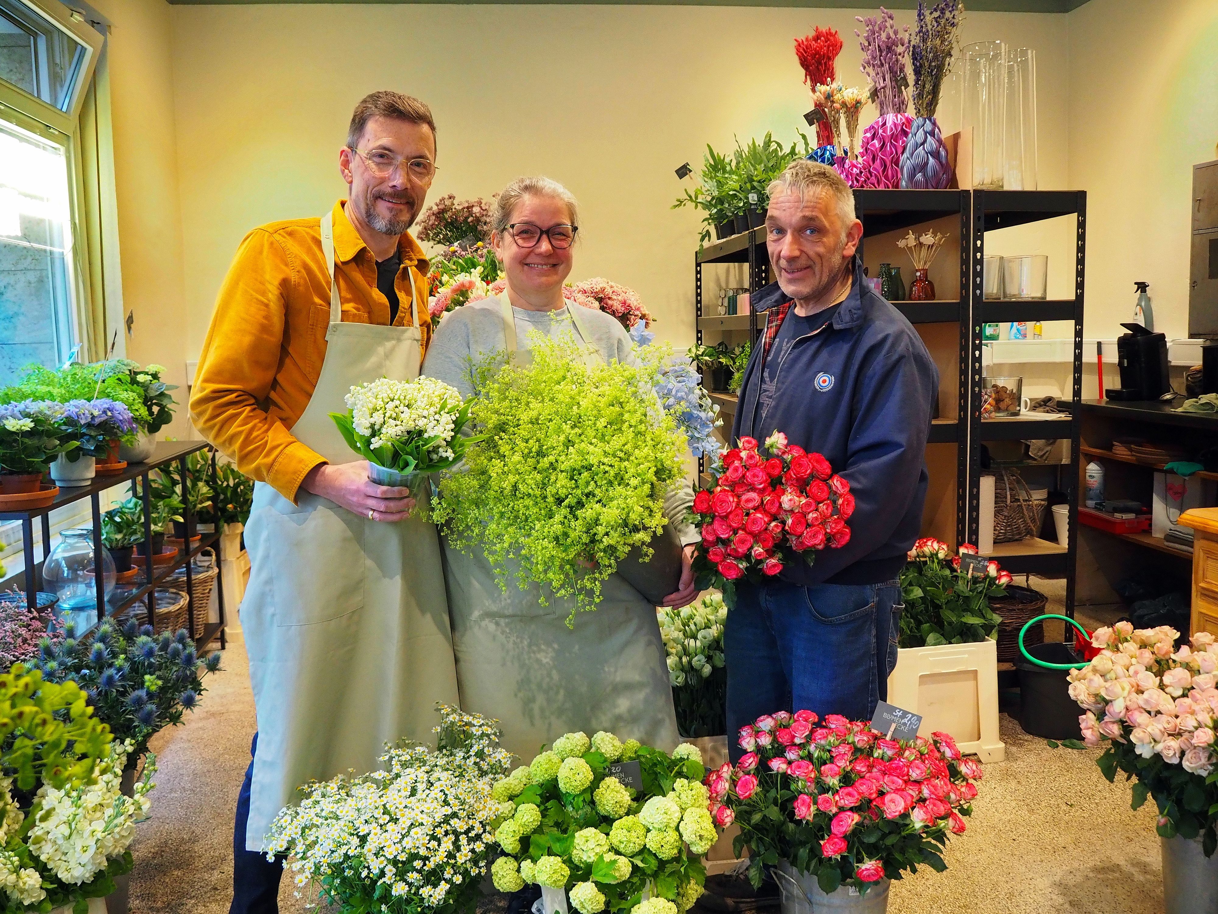 Zwei Männer und eine Frau stehen nebeneinander in einem Blumengeschäft.