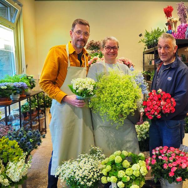 Zwei Männer und eine Frau stehen nebeneinander in einem Blumengeschäft.