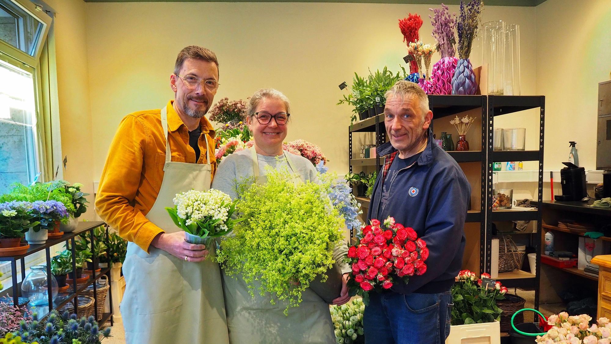 Zwei Männer und eine Frau stehen nebeneinander in einem Blumengeschäft.