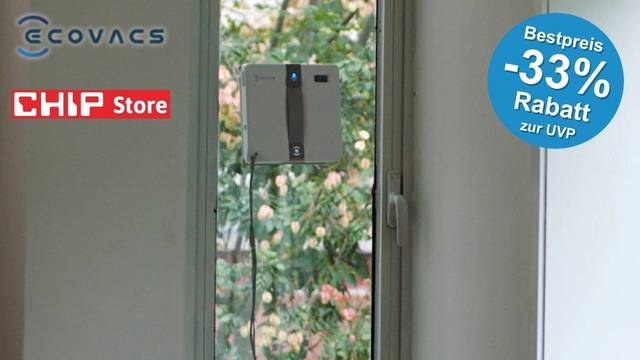 Der grau-schwarze Ecovacs Winbot Mini Fensterputzroboter haftet an einer schmalen Balkontür mit Blick auf grüne Bäume und Sträucher. Links oben das Ecovacs-Logo sowie das rote CHIP Store-Logo. Rechts oben blauer Button.