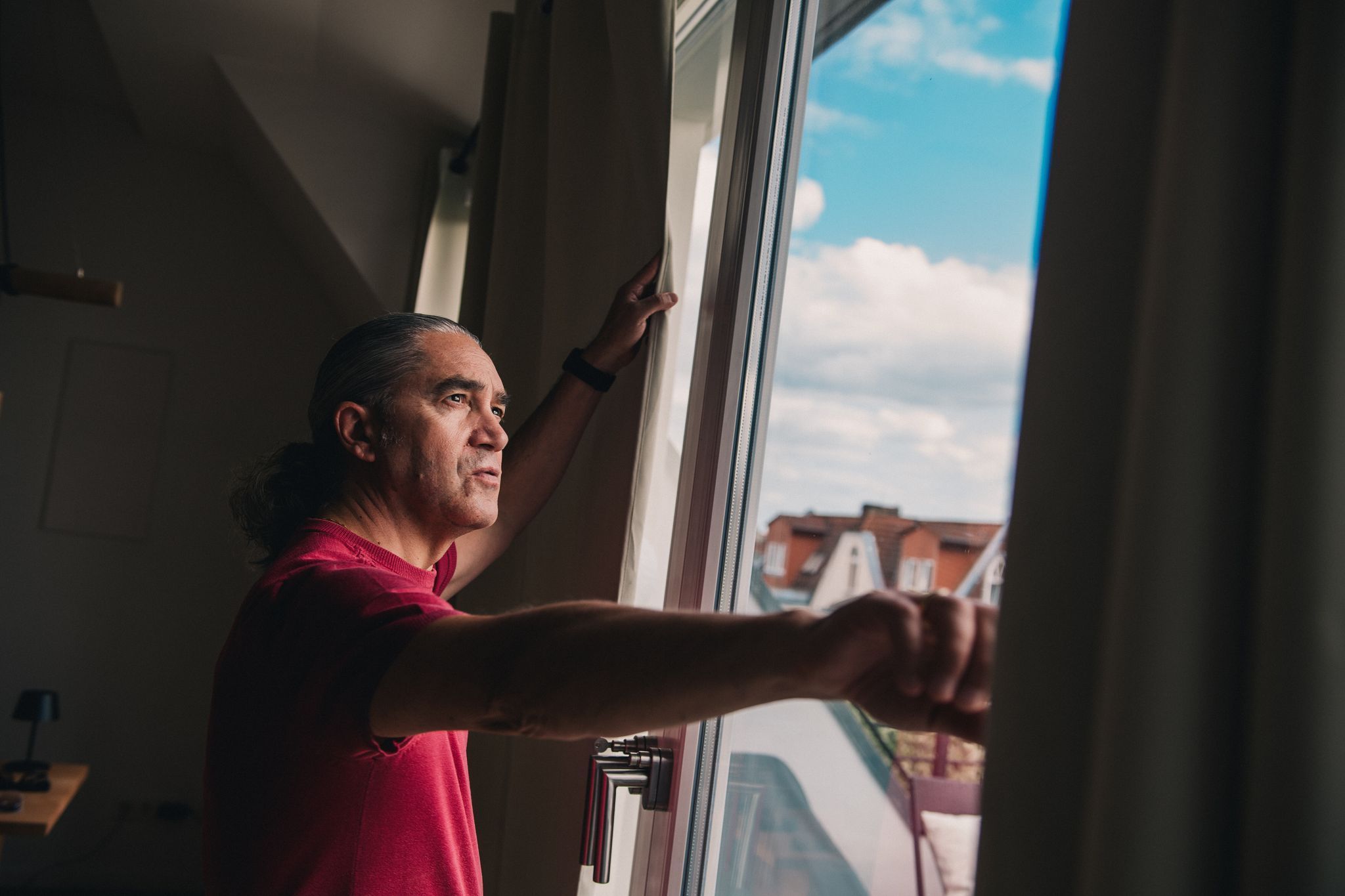 Mann steht vor dem Fenster seiner Wohnung