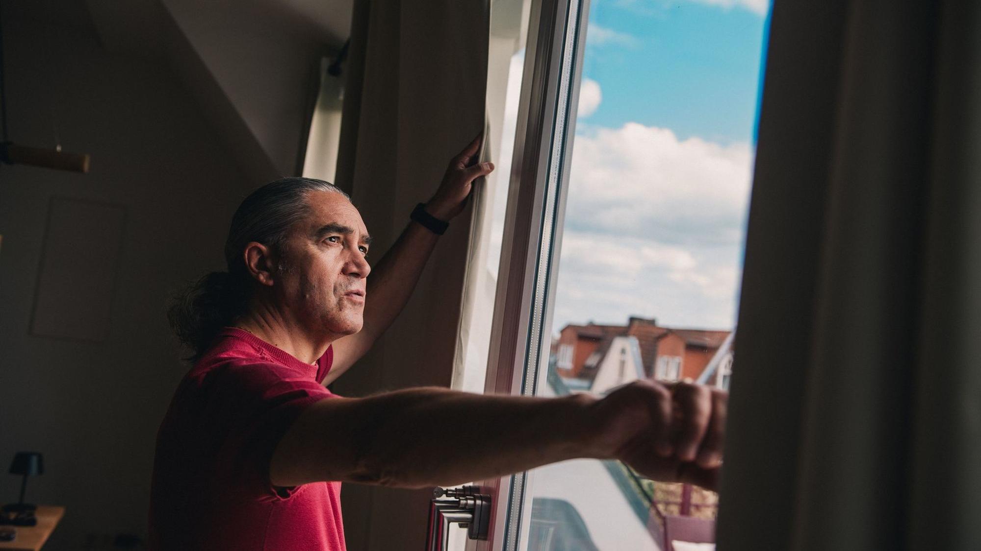 Mann steht vor dem Fenster seiner Wohnung