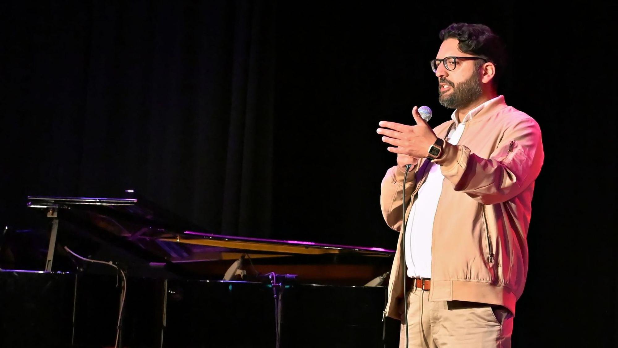 Amir Shahbazz bei seinem Auftritt in Euskirchen. Er trägt Vollbart, eine Brille sowie eine beige Hose und ein weißes Hemd unter einer beigen Jacke.