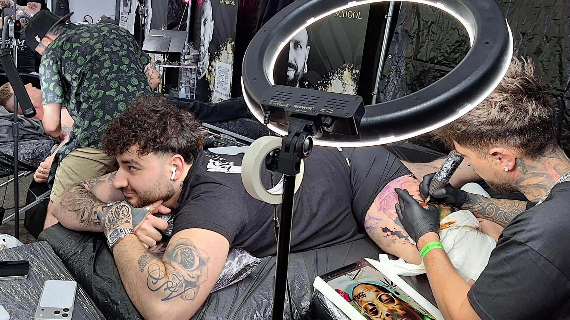 Ein Mann liegt auf dem Bauch, während ihm ein Tätowierer ein Tattoo auf den Oberschenkel sticht.