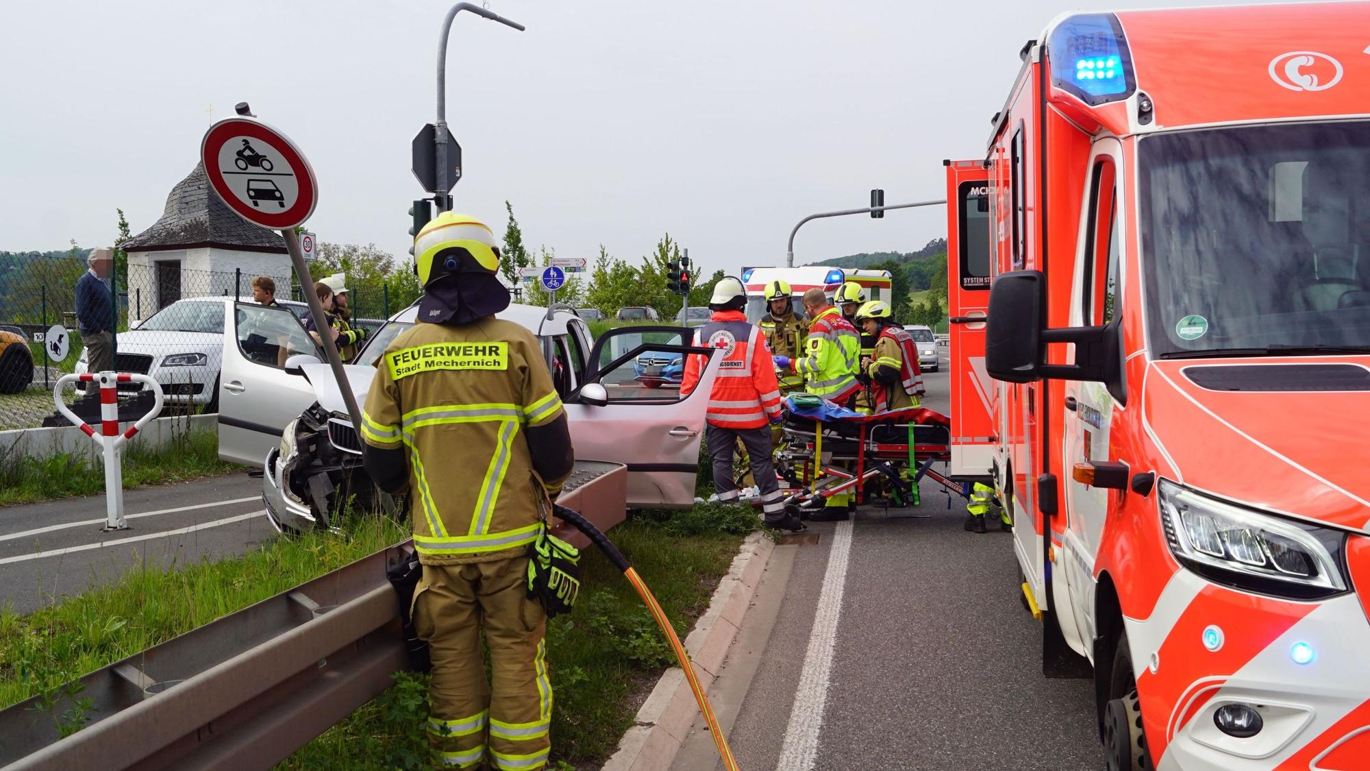 Rechts ist ein Rettungswagen zu sehen, daneben stehen Einsatzkräfte an einem verunfallten Auto.