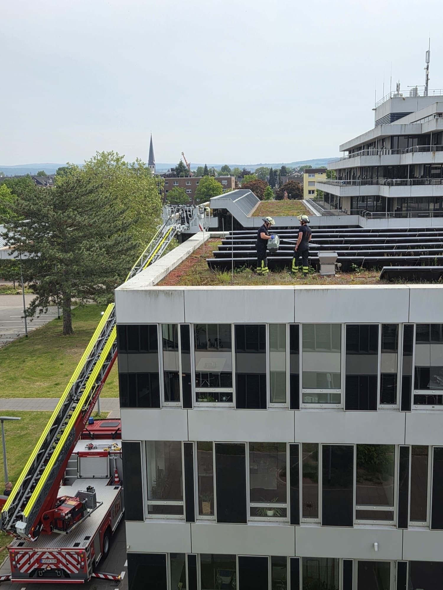 Zwei Feuerwehrleute stehen auf dem Dach des Kreishauses in Euskirchen. Links ist der Korb der Drehleiter zu sehen.