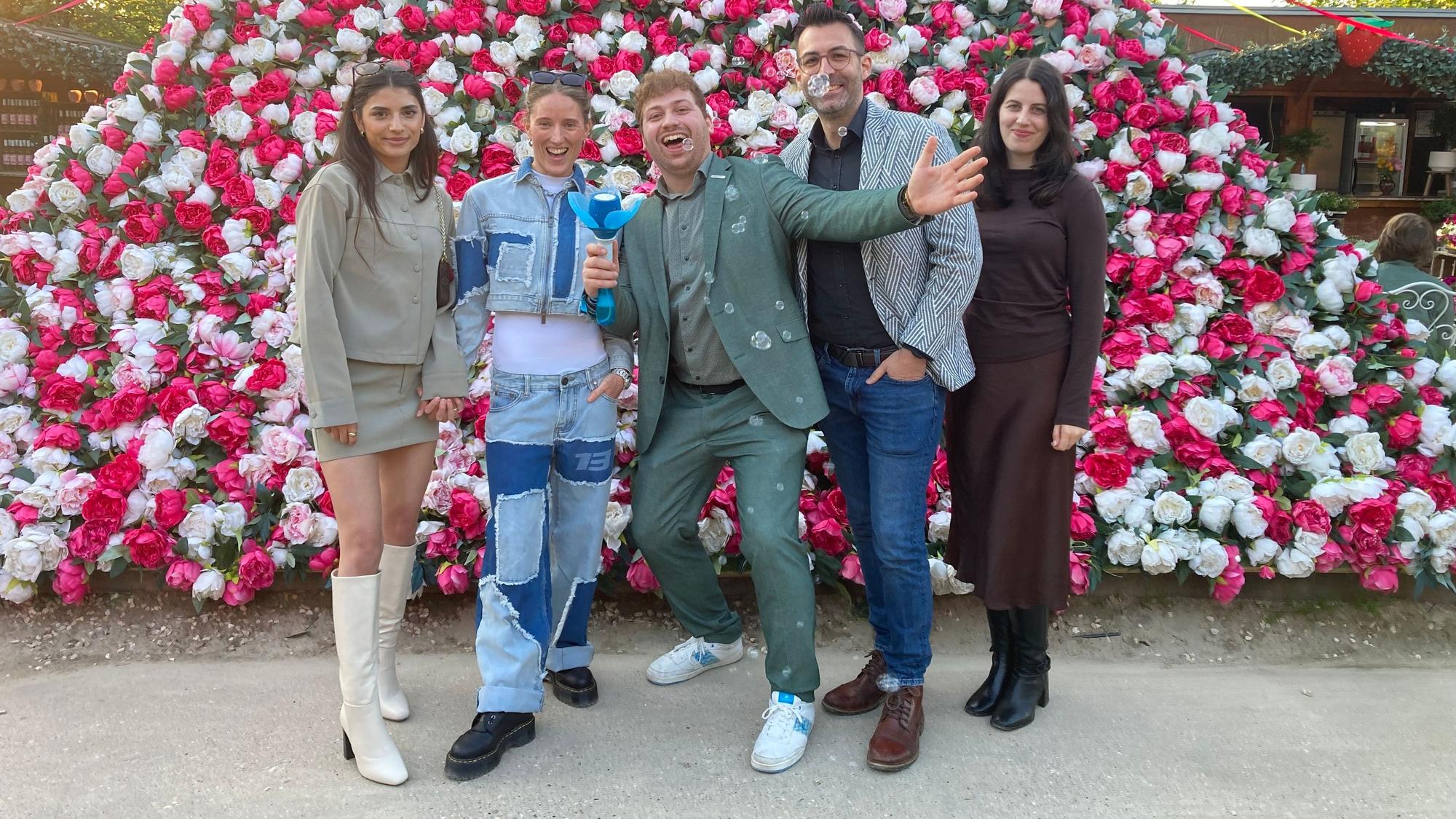Auf dem Bild ist eine Gruppe von jungen Leuten zu sehen, die vor einer Pyramide aus Blumen stehen.