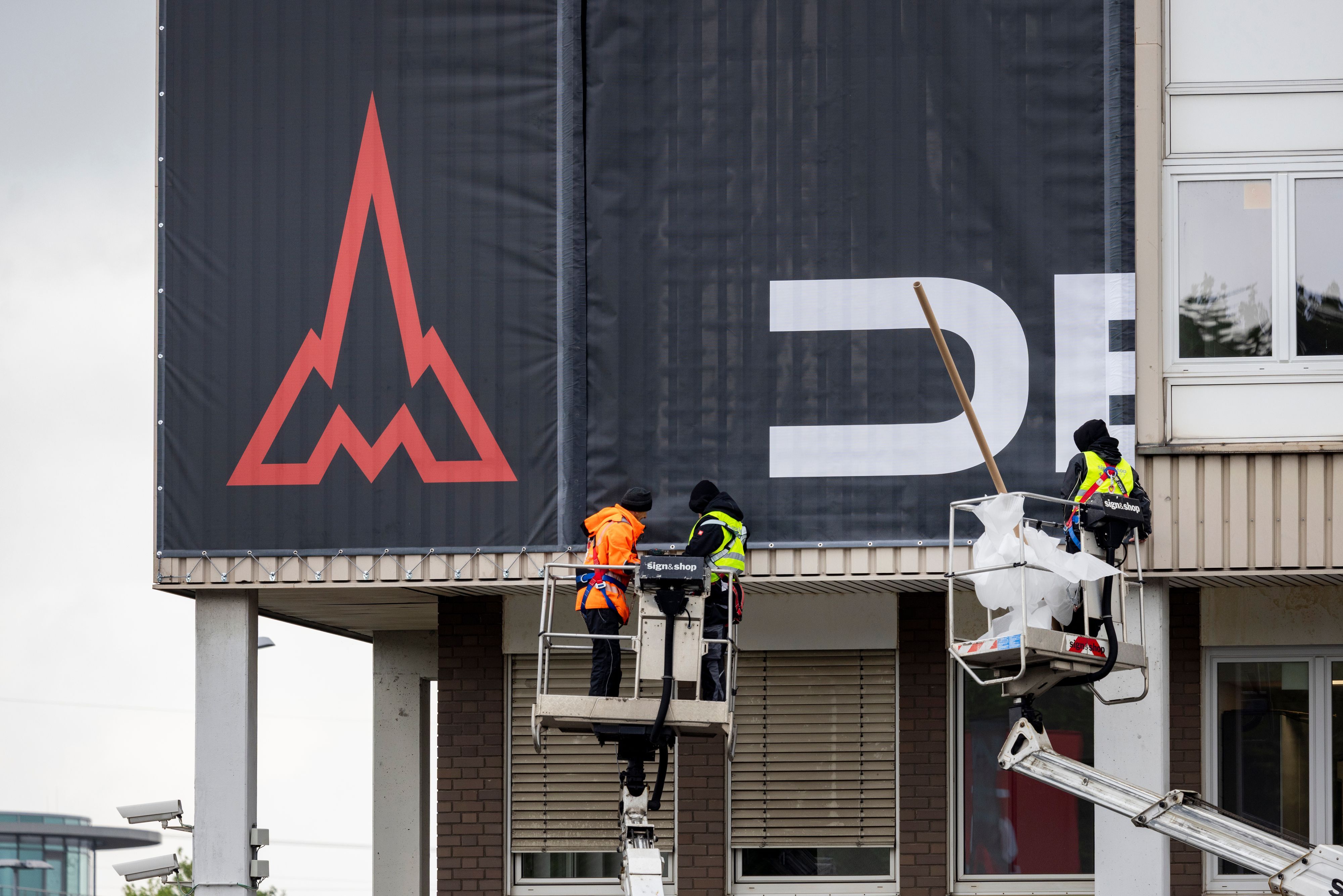 Arbeiter auf Kränen befestigen Fassadenbanner mit dem neuen Deutz-Logo am Hauptgebäude in Köln-Porz