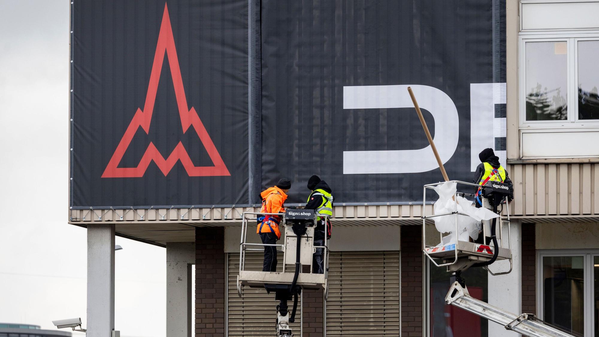 Arbeiter auf Kränen befestigen Fassadenbanner mit dem neuen Deutz-Logo am Hauptgebäude in Köln-Porz
