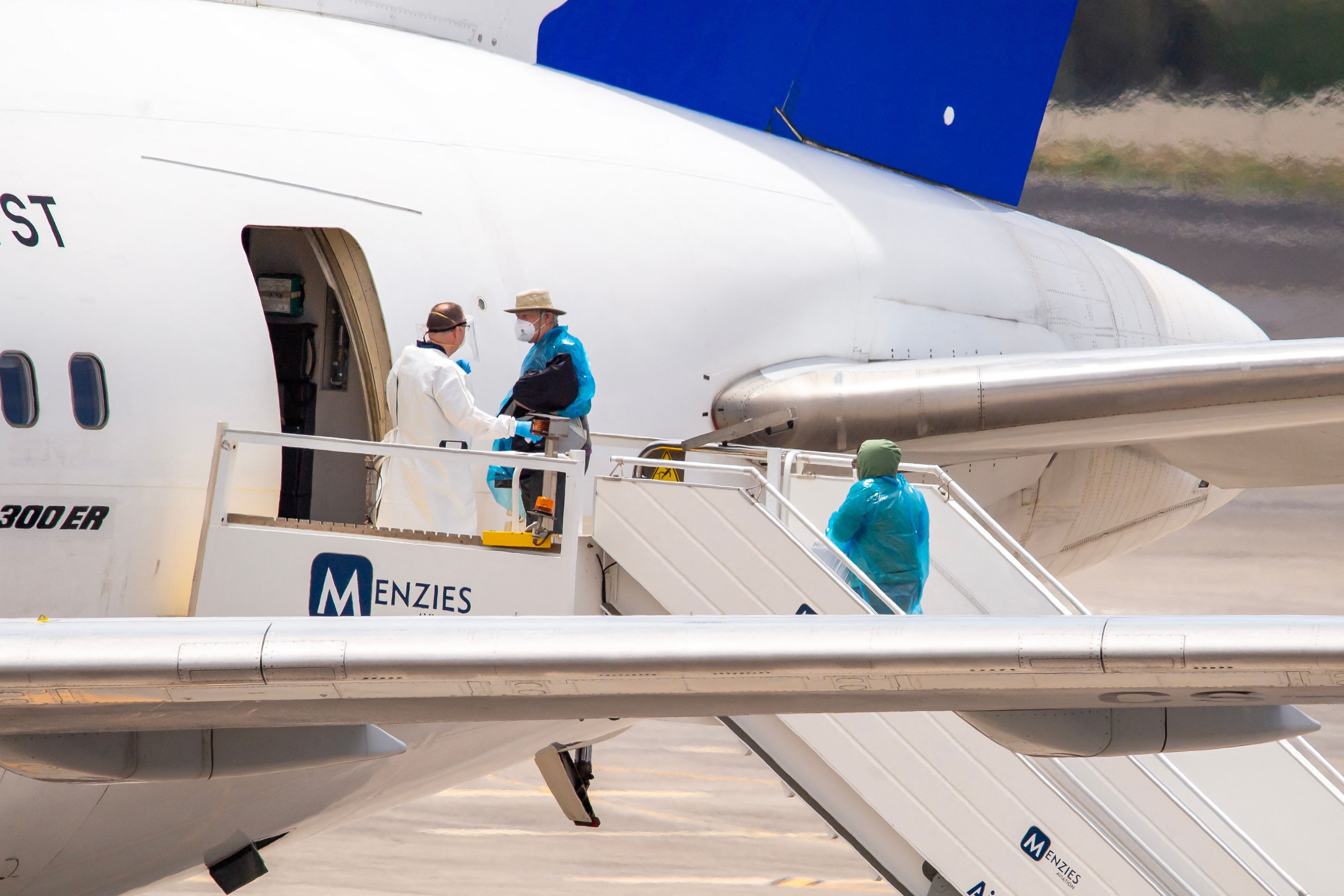 Passagiere in Schutzanzügen betreten ein Flugzeug.