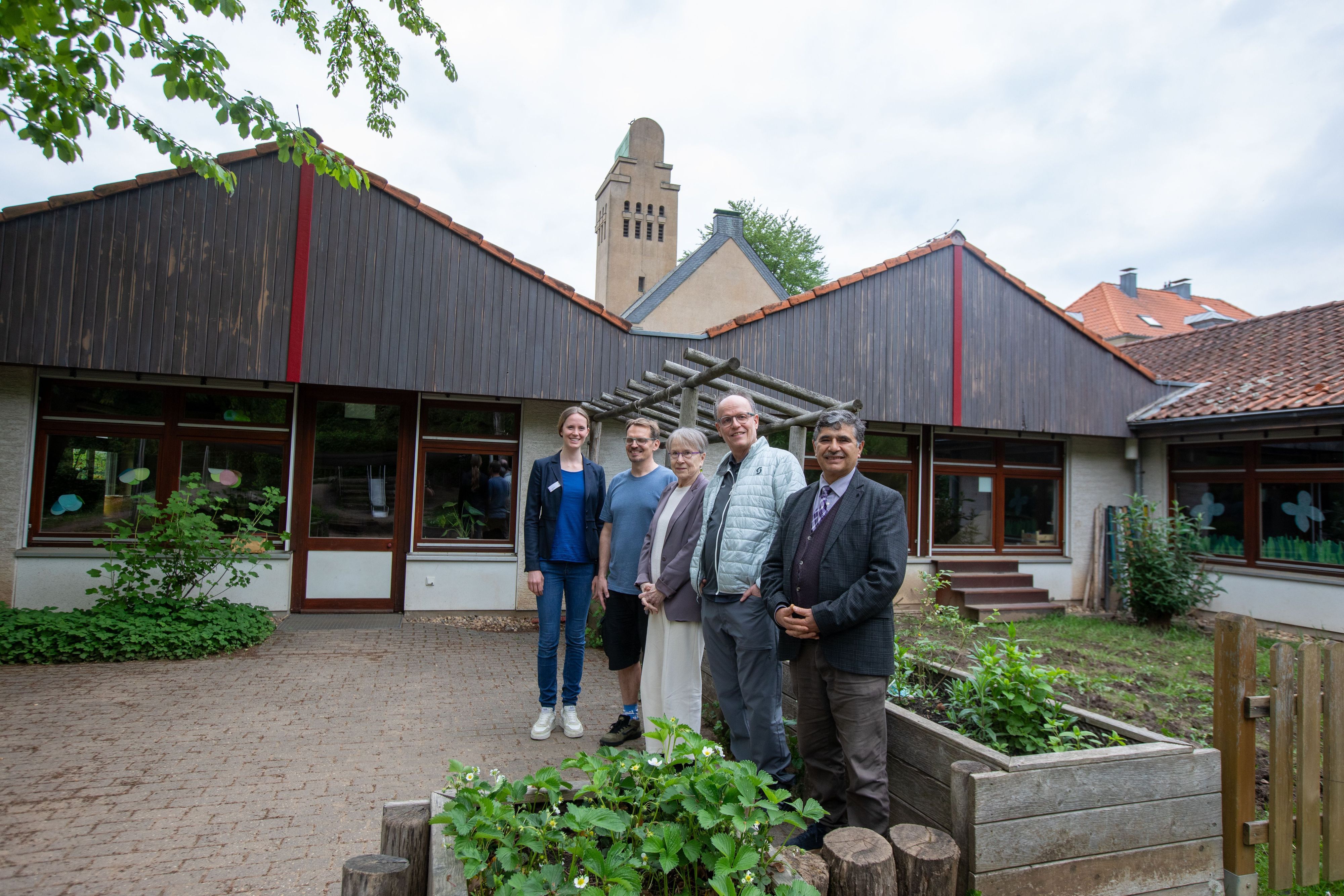 Drei Männer und zwei Frauen stehen im mit Hochbeeten gestalteten Bereich vor einer Kita.