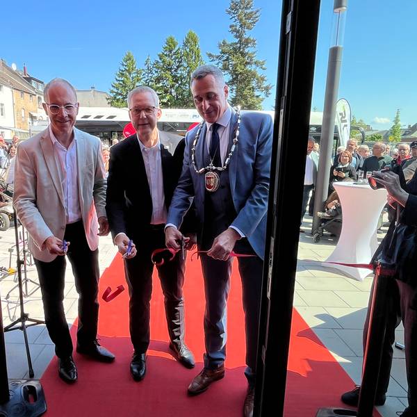 Auf dem Bild sind drei Männer mit Sakkos zu sehen, die ein Einweihungsband durchschneiden.