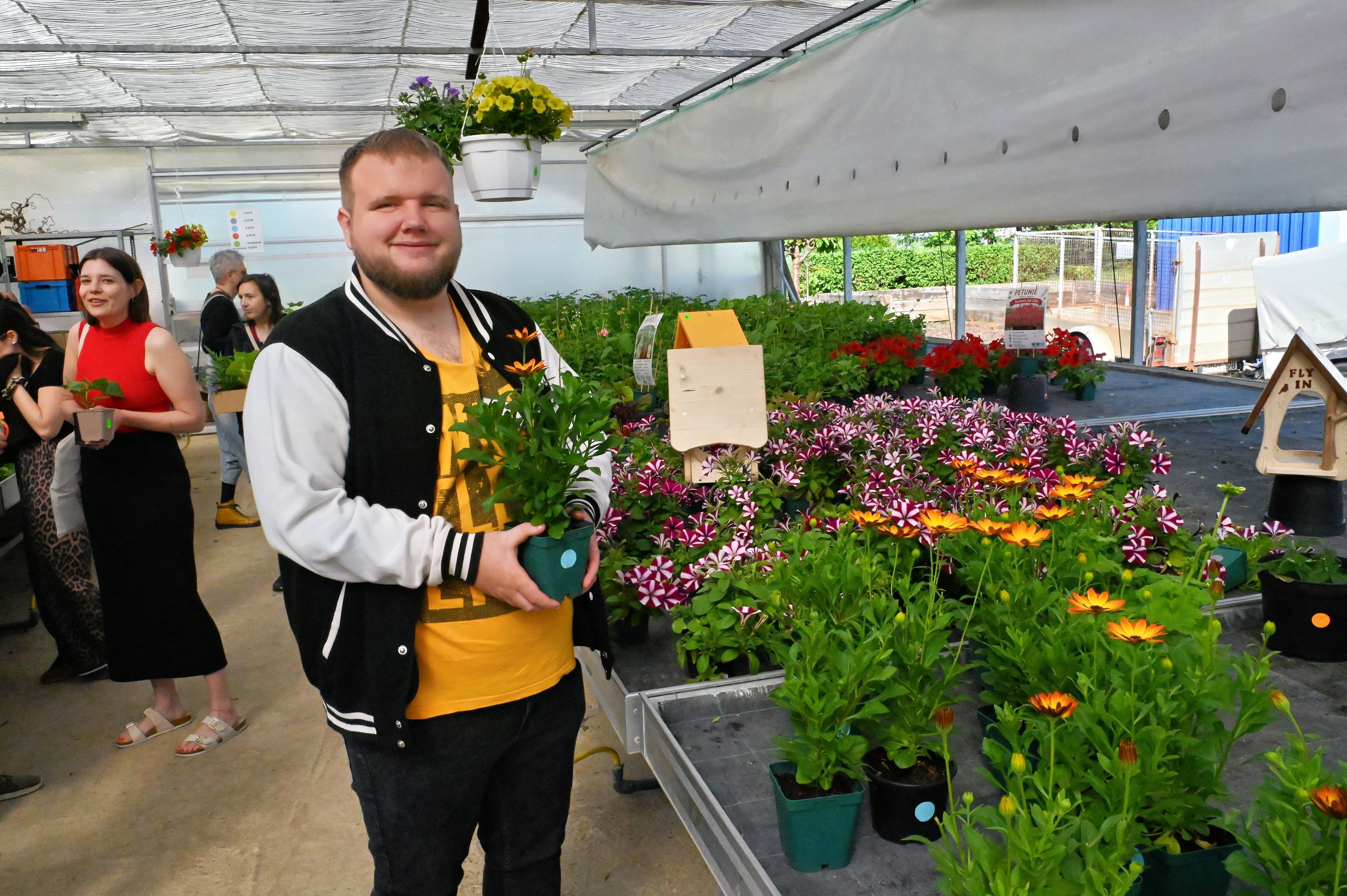 Sebastian Tholl hält eine Blume in der Hand, neben ihm stehen weitere blühende Pflanzen.