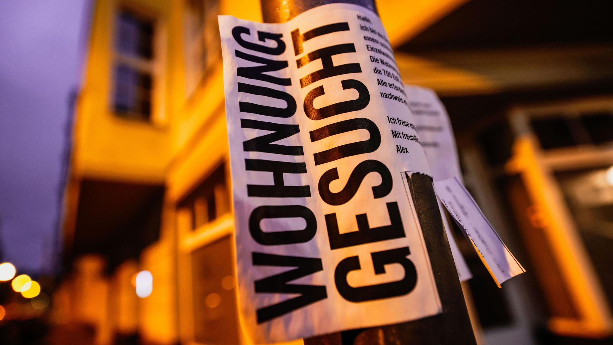 Ein Zettel mit der Aufschrift „Wohnung gesucht“ hängt vor Wohnhäusern in Köln.